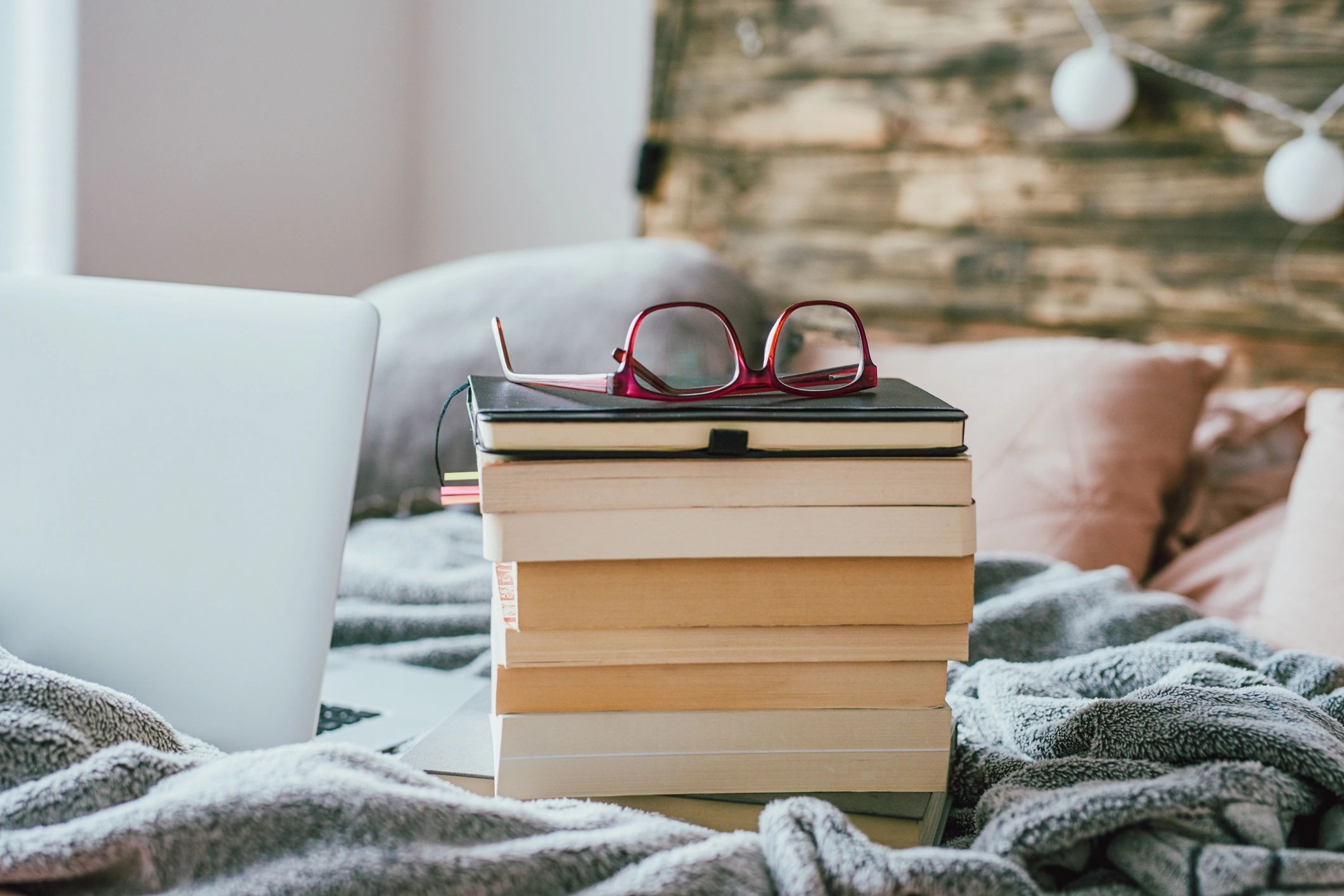 Stack of books with glasses and a laptop in warm light