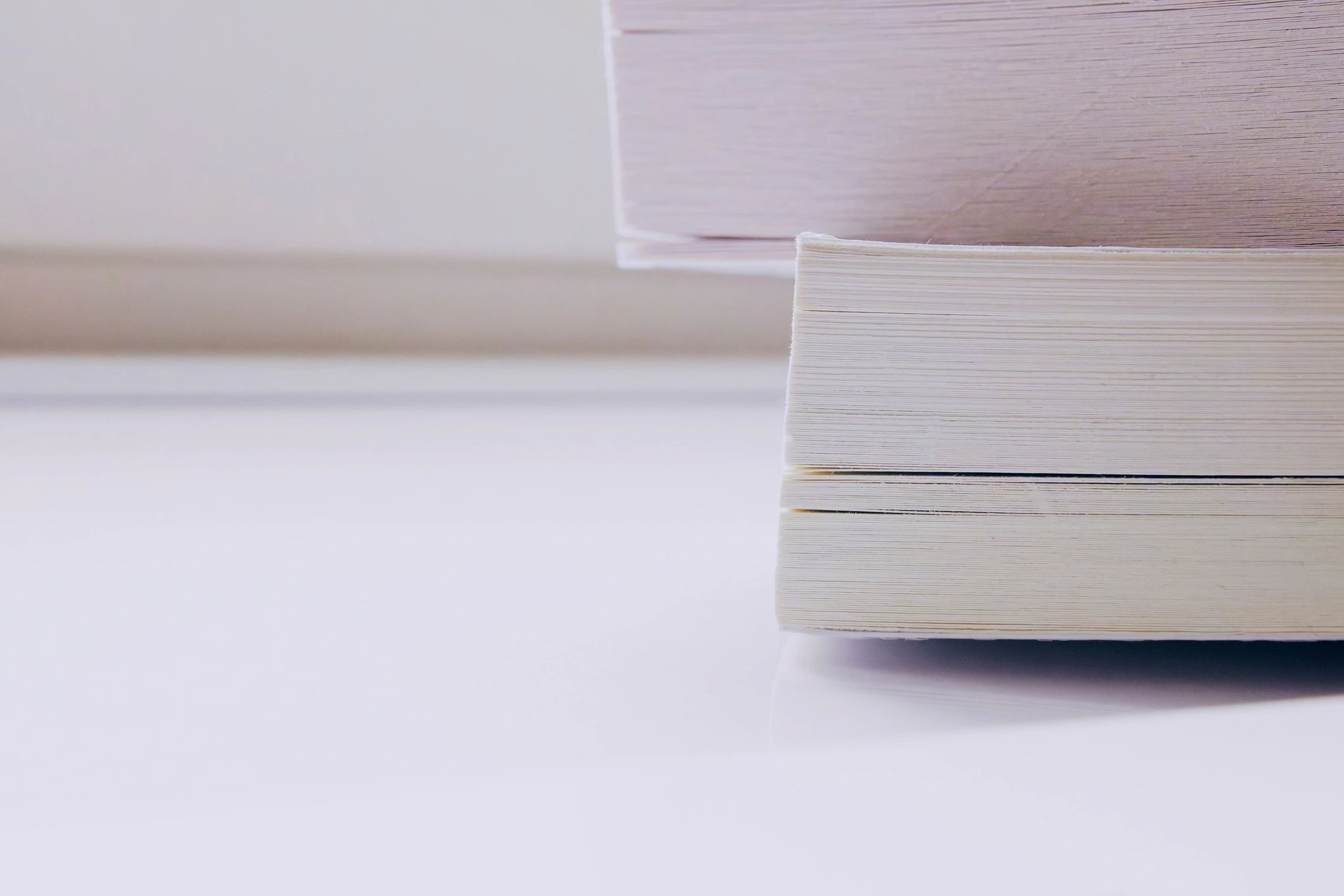 Minimal stack of white books in soft natural light against a white wall