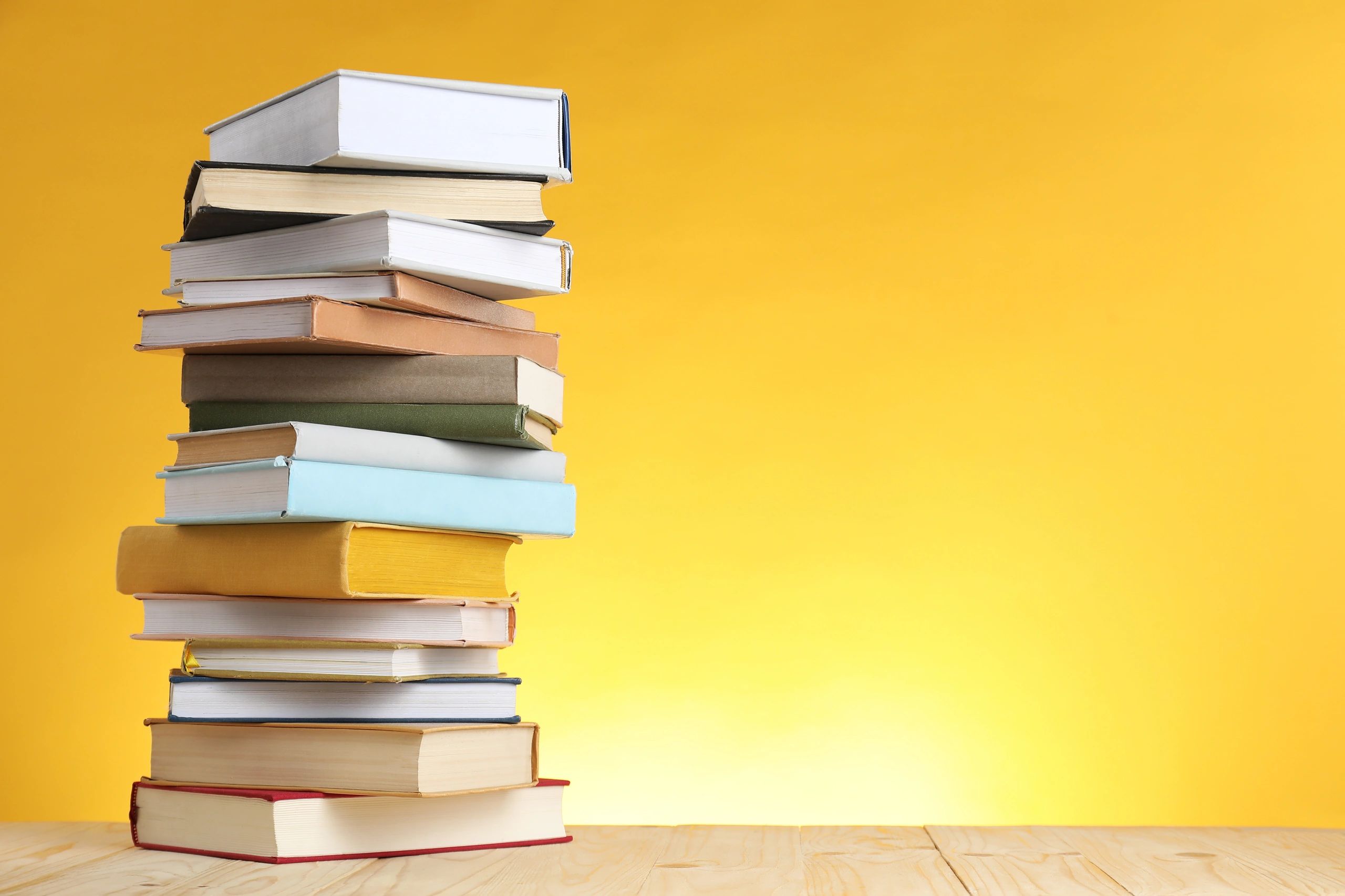 Stacked books on a table against a yellow background with space for text